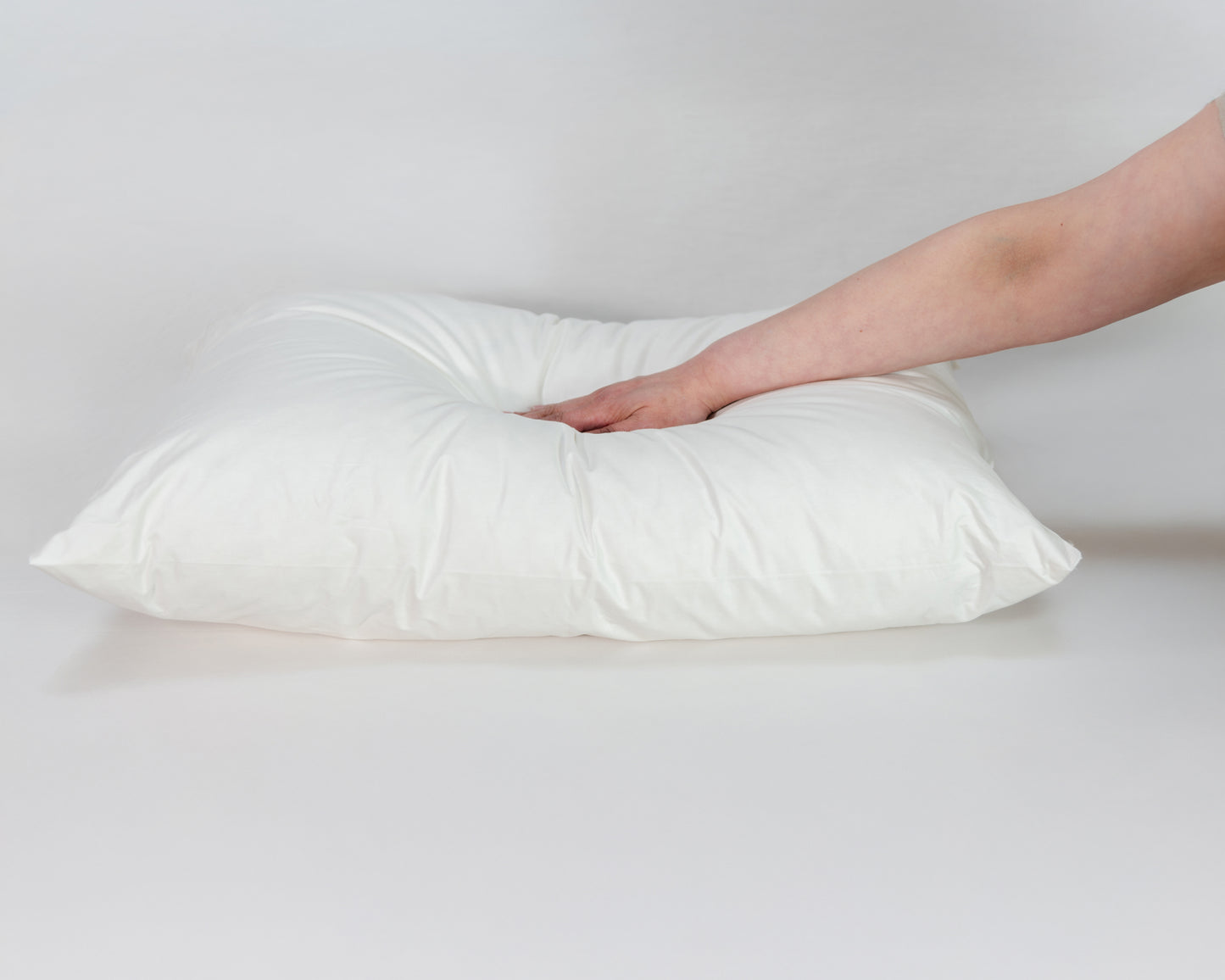 Mano presionando la almohada suave de La Casa de los Gansos, destaca su textura blanda y envolvente