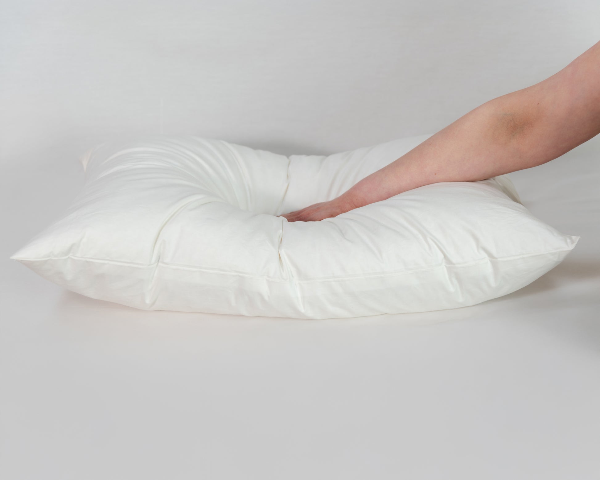 Mano presionando la almohada duvet de La Casa de los Gansos, resalta su rebote y firmeza controlada
