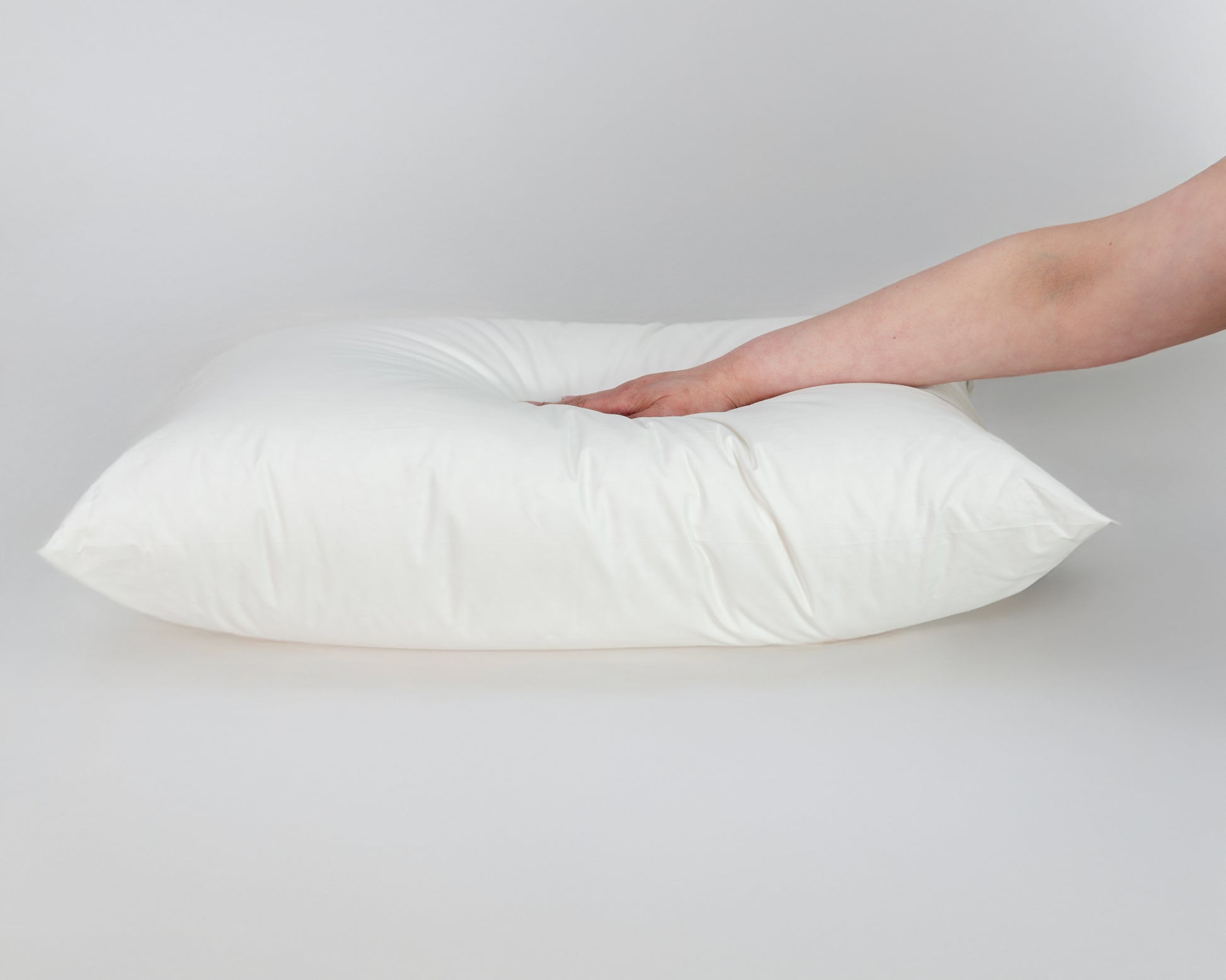 Mano presionando la almohada firme de La Casa de los Gansos, evidencia su resistencia y soporte elevado